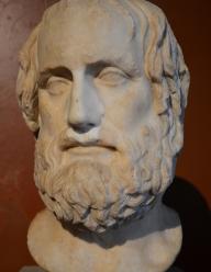 An ancient marble bust of a man, shaggy hair and a beard. He is Euripides.