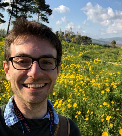 A man with glasses smiling in front of wildflowers