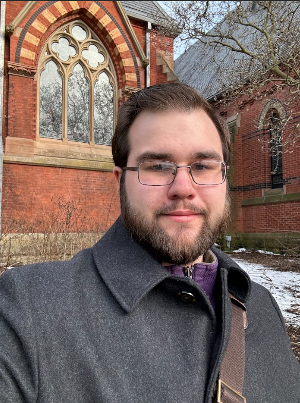 Terek stands in front of a brick building with an ornate arched window.